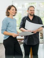 Zwei Mitarbeitende stehen im Büro und schauen sich ausgedruckte Plakate an